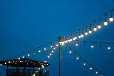 Sıcak bir gece etkinliği için ışık saçan ampuller ya da fenerler dizili açık hava dekorasyonu. Sıcak, atmosferik ve romantik bir ortam..