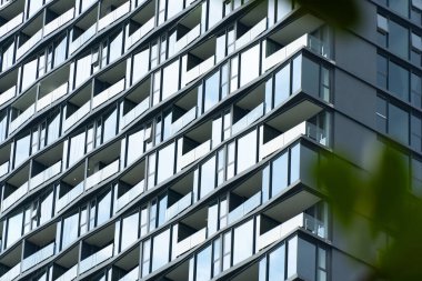 Camdan yapılmış büyüleyici geometrik desenli modern bir ofis binasının çarpıcı mimari cephesi ve çevre şehrin ufuk çizgisini yansıtan temiz, minimalist tasarımı..