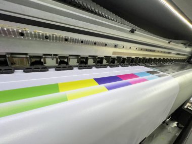Çıktı medyasında çeşitli renk desenleri ve çizgilerle modern bir ticari fotoğraf stüdyosundaki çok renkli baskı makinesi, otomatik ve yüksek teknolojili bir endüstriyel baskı sürecini tasvir ediyor.