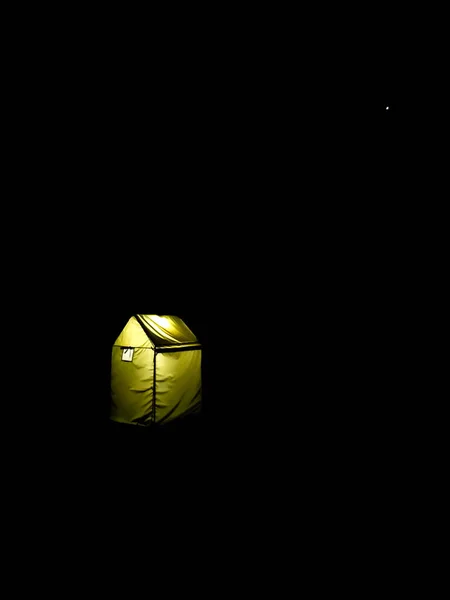 A camping tent glowing in a pitch dark surround at a base camp in the lower Himalayan Region In Uttarakhand India.