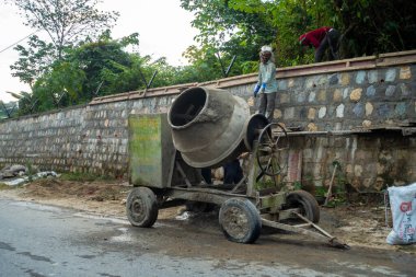 28 Haziran 2023, Uttarakhand, Hindistan. Yol boyunca taştan istinat duvarı inşaatı. Karıştırma makinesi ve işçilerle birlikte..