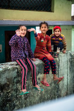 14 Ekim 2022 Uttarakhand, Hindistan. Renkli elbiseli genç Hintli kızlar, tuğla duvarda oturmuş eğleniyorlar. Neşeli ve canlı anlar yakalandı..
