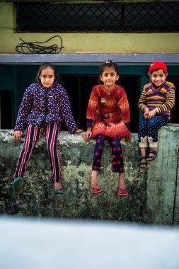 14 Ekim 2022 Uttarakhand, Hindistan. Renkli elbiseli genç Hintli kızlar, tuğla duvarda oturmuş eğleniyorlar. Neşeli ve canlı anlar yakalandı..
