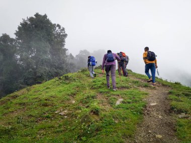 14 Ekim 2022, Uttarakhand Hindistan. Sırt çantalı ve bastonlu maceraperest bir yürüyüş grubu Hindistan 'ın Uttarakhand, Nag Tibba' da sisli ve dik bir dağı fethediyor. Heyecanlı bir keşif gezisi.