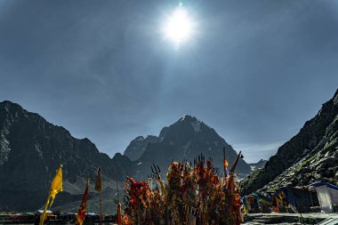 July25th2024, Himachal Pradesh, India. Religious red cloths (chunri) and tridents (trishul), symbols of Lord Shiva, against Kailash Parvat during the Mani Mahesh Kailash Yatra, a Hindu and Buddhist pilgrimage. clipart