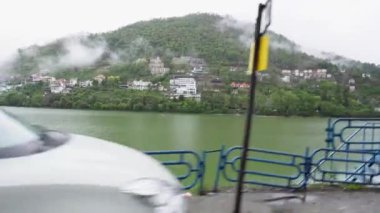 Bhimtal Gölü 'nün engin uzunluğu, yeşil su ve çevresindeki uçurumların manzarası Almora, Uttarakhand, Hindistan' da hareket halindeki bir araçtan görülüyor..