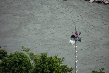 An emergency siren and announcement tower with loudspeakers situated near a dam channel in Himachal Pradesh, India, for safety announcements during high water events. clipart