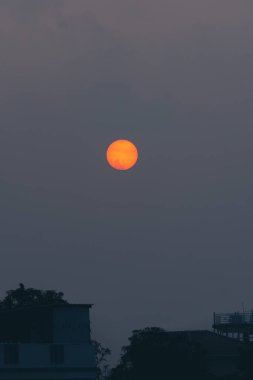 Puslu bir gökyüzünde yuvarlak turuncu bir güneş, Uttarakhand, Hindistan 'a batmadan dakikalar önce. Doğal ortamda alacakaranlığın huzurlu ve huzurlu bir tasviri..