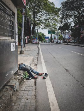 27 Mayıs 2025 dehradun şehri Hindistan. Sarhoş evsiz insan ağaçlar ve binalarla dolu boş bir caddenin yanında, sessiz bir kaldırımda yatıyor.