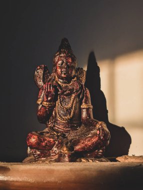 2 Temmuz 2025 Dehradun Uttarakhand Hindistan. Ilık aydınlıkta oturan yıpranmış bir tanrı heykeli, bir gölge.