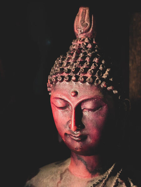 Close-up of a red Buddha statue with serene expression in dim lighting.