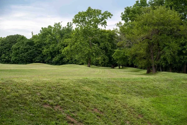 Native American Hopewell Culture prehistoric Earthworks burial mounds in Mound City park Ohio. Ancient small circular mounds with a long mound surrounding. Grass is neatly trimmed with trees and