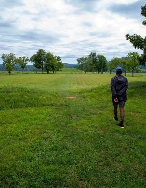 A young man walks toward the Native American Hopewell Culture prehistoric Seip Earthworks burial mound in Ohio. Ancient large long mound. Grass is neatly trimmed with trees and dramatic sky. Copy
