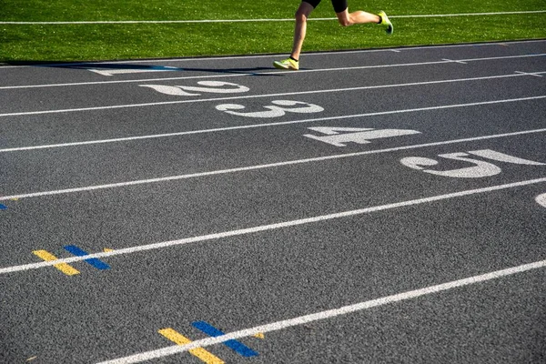 A runner on a gray athletic running track with large white numbers. Runner races over numbers with copy space. Selective focus on track for excellent track and field background.