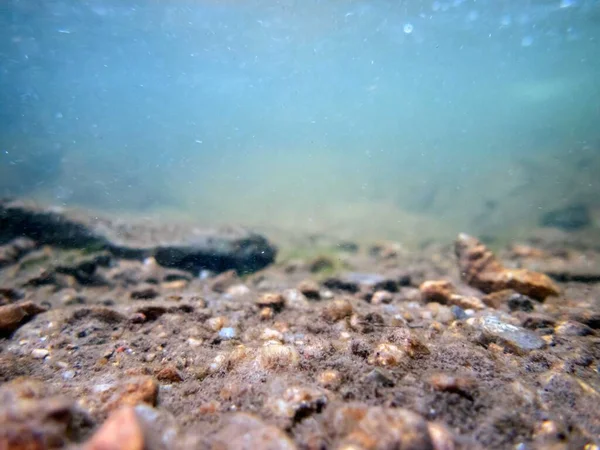 Blue-green flowing water ripples and bubbles over colorful textured rocks and silt in a clean beautiful Pennsylvania waterway. Serene image of healthy underwater environment. Great background with