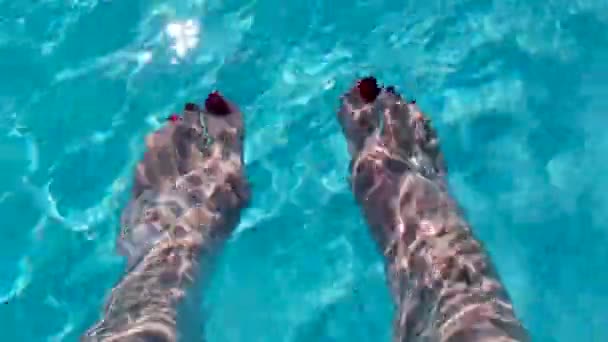 きれいな青いプールの水は 波打つように太陽の下で輝き 水の中を上下に同時に動く女性の足の上を流れます 高エネルギーの休暇のイメージは爽やかでリラックスしていて — ストック動画