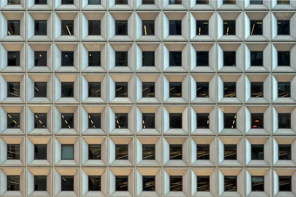 一幢摩天大楼正面的几何建筑背景 该大楼有一排相同的窗户 内部有灯光图案 — 图库照片