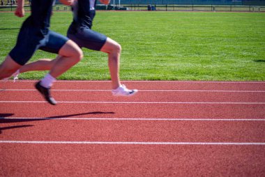 Açık hava atletizm pistinde beyaz şerit çizgileri ve yeşil çimen arka planı olan iki kişi yarışıyor..