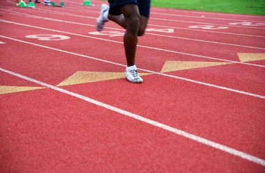 Yalnız Afrikalı Amerikalı koşucu kırmızı atletik bir spor pistinde ve saha pistinde fotokopi alanı olan bir yolda yarışıyor..