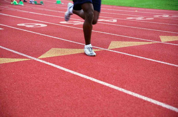 Lone African American runner racing in a numbered lane on a red athletic sports track and field stadium track outdoors with copy space.