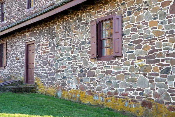 美丽的美国殖民时期的石头房子是用五彩斑斓的宾夕法尼亚田野石建成的 外墙有古窗 百叶窗和红门 有复制空间 没有人 Daniel Boone Homestead — 图库照片