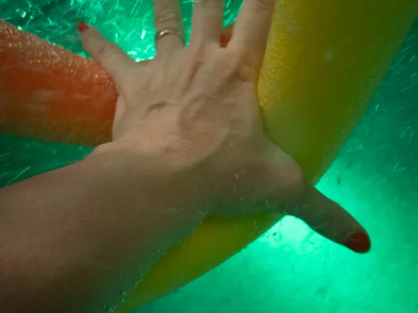アクアエアロビクスプールの麺を把握するために精力的にプールの水を介して到達女性の手のクローズアップイメージ — ストック写真