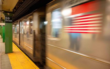 59. caddedeki New York metro istasyonunda yeşil sütun ve sarı güvenlik hattı var. Metro vagonu hareket bulanıklığıyla geliyor ya da kalkıyor.