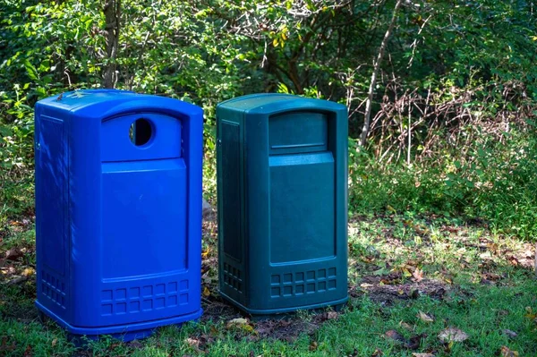 Blue and green recepticles for trash and recycling on a rural hiking trail in the green leaft woodland. Environmental concepts with no people and copy space.