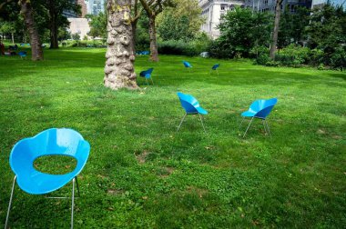 Kamu parkının yeşil çimenleri Battery Park New York şehri boş mavi bahçe sandalyeleri, eğri büğrü ağaçlar ve arka planda şehir binaları. Kopyalama alanı olan kimse yok.