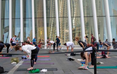 Bir grup insan, Dünya Ticaret Merkezi 'nin dışındaki Oculus alışveriş merkezi ve metro istasyonunda yoga dersi veriyor. Kaldırımdaki yoga minderleri ve yoga yapan insanlar gökdelenlerle poz veriyor. Oculus pencerelerine yansıyor. Sadece editör kullanımı.