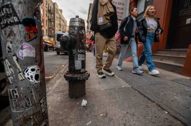 New York, New York, ABD 11-09-2023 Alçak açılı manzara yayalar şehir caddesinde yangın musluğu ve sokak sanatı ile kaplı elektrik direği ile. Kopyalama alanı ile seçmeli odak. Sadece editör kullanımı.