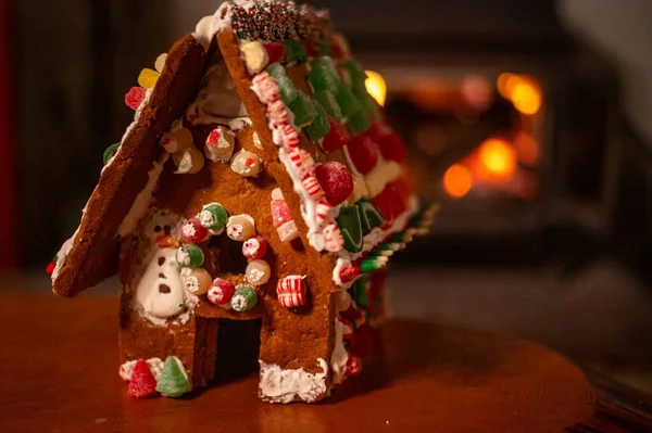 Bokeh firepace background with copy space and no people. Homemade childs gingerbread house in foreground with candy and icing warm welcoming holiday scene