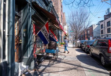 Philadelphia, PA, USA 03-14-2024. Bir kişi, şehir merkezindeki Bainbridge Caddesi 'nde Anastacia' s Antiques 'in önünde bayrakları olan bir antikacıya giriyor. Öndeki kaldırımda sergilenen antikalar, mavi gökyüzü, bir müşteri,