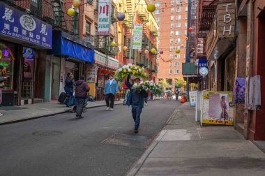 New York, New York, ABD 11-09-2023 Bir çiçekçi teslimatçı Çin Mahallesi 'nde yayalar ve işlek şehir sokak manzaralı iki büyük çiçek sergisi taşıyor. Sadece editör kullanımı.