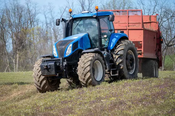 农业拖拉机拖动粪肥播种机使具有树木背景和复制空间的农田施肥 — 图库照片