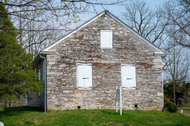 Douglasville, PA, ABD 04-10-2024. Exeter Meetinghouse. Pensilvanya 'nın kırsal kesimlerinde yeşil çimen manzarasında antika pencereleri ve panjurları olan küçük taş bir Quinaker toplantı evi. Sadece editör kullanımı