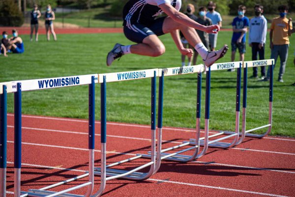 Wyomissing, PA, USA 04-13-2021 Young student athlete leaps over a hurdle on an athletic running track in an outdoor track and field event competition. Motion blur and defocused spectators in