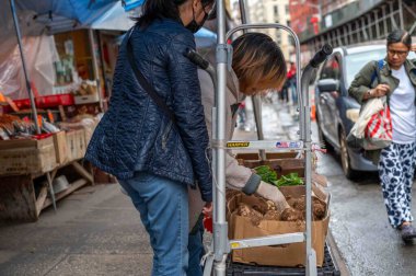 New York, New York, ABD 05-15-2024 Kadınlar Çin Mahallesi 'ndeki bir Asya marketinin önündeki kaldırım vitrinindeki Asya sebze kutularına bakıyorlar. Sadece editör kullanımı.