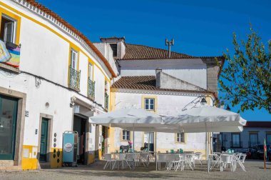 Evora, Portekiz, 11-19-2024 beyaz masa ve sandalyeler beyaz masa şemsiyelerinin altında güneşli bir günde kaldırım taşı kaldırımdaki güzel bir kafede. Kopya alanı olan mavi gökyüzü