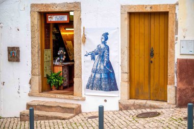 Silves, Portugal, 11-24-2024, Ancient steps and stone doorways on cobblestone street with beautiful art sign and ceramic shop storefront beside old closed wooden door clipart