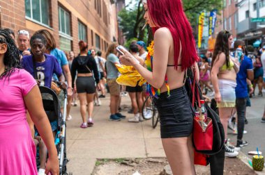 Philadelphia, PA, USA 06-02-2024 Havalı kadın sigara kontrolü yapıyor Philadelphia 'daki Onur Festivali' nde akıllı telefon, renkli kıyafetler ve kalabalık kızıl saçlı festival caddesi geçmişi.