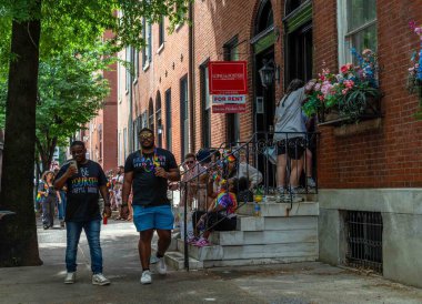 Philadelphia, PA USA, 06-02-2024 kalabalık bir caddede yürüyen iki havalı adam Center City, Pride Fest 'teki tarihi tuğla evlerin önünden geçiyor, verandalardaki renkli sahne insanları. Güzel insanlar..