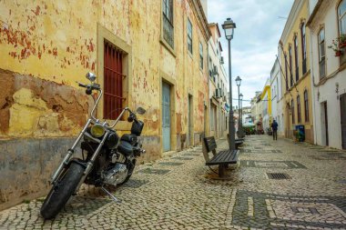 Silves, Portekiz, 04-17-2025 Çok güzel bir Algarve caddesinde eski binaları, evleri ve Mozaik kaldırımları ve bankları olan dükkanları olan bir motosiklet helikopteri.