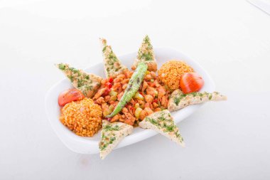 Tavada özel marine edilmiş kuzu eti, bulgur pilavı, domates ve pita ekmeği ile servis edilir..