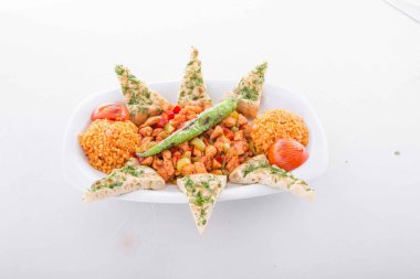 Tavada özel marine edilmiş kuzu eti, bulgur pilavı, domates ve pita ekmeği ile servis edilir..