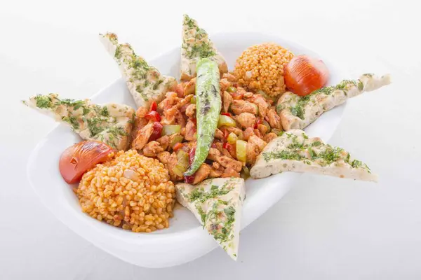 Tavada özel marine edilmiş kuzu eti, bulgur pilavı, domates ve pita ekmeği ile servis edilir..
