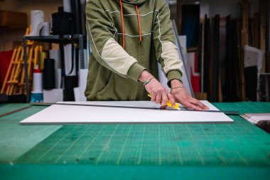 Crop anonymous male worker in casual clothes cutting board with knife at workbench in printing industry