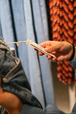 Giyim mağazasından alışveriş yaparken etiketi tutan ve fiyatı kontrol eden isimsiz biri.