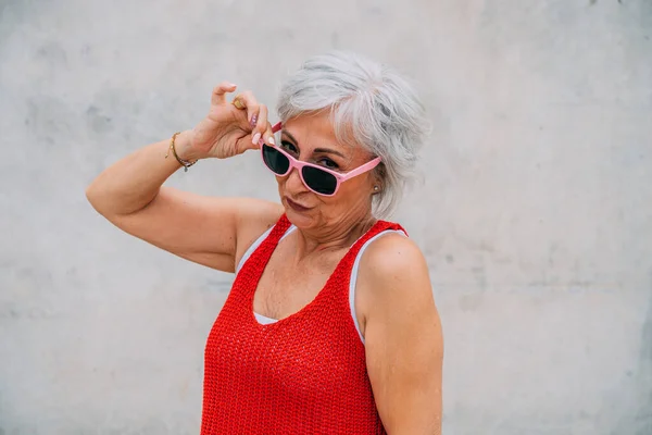 Dojrzała Kobieta Czerwonej Dzianinie Dopasowuje Okulary Przeciwsłoneczne Dąsając Się Wargami — Zdjęcie stockowe