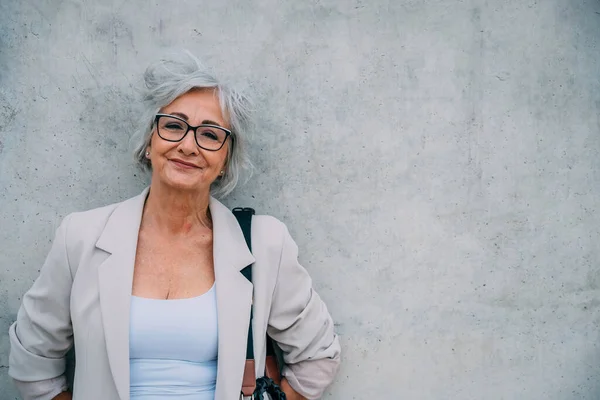 Pozytywna Seniorka Siwymi Włosami Okularach Eleganckimi Ubraniami Opierająca Się Obskurnej — Zdjęcie stockowe